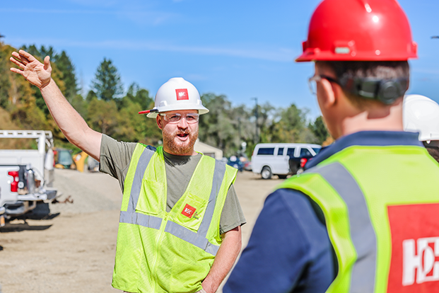 Man in a construction uniform looking at another person in a construction uniform and gesturing. 