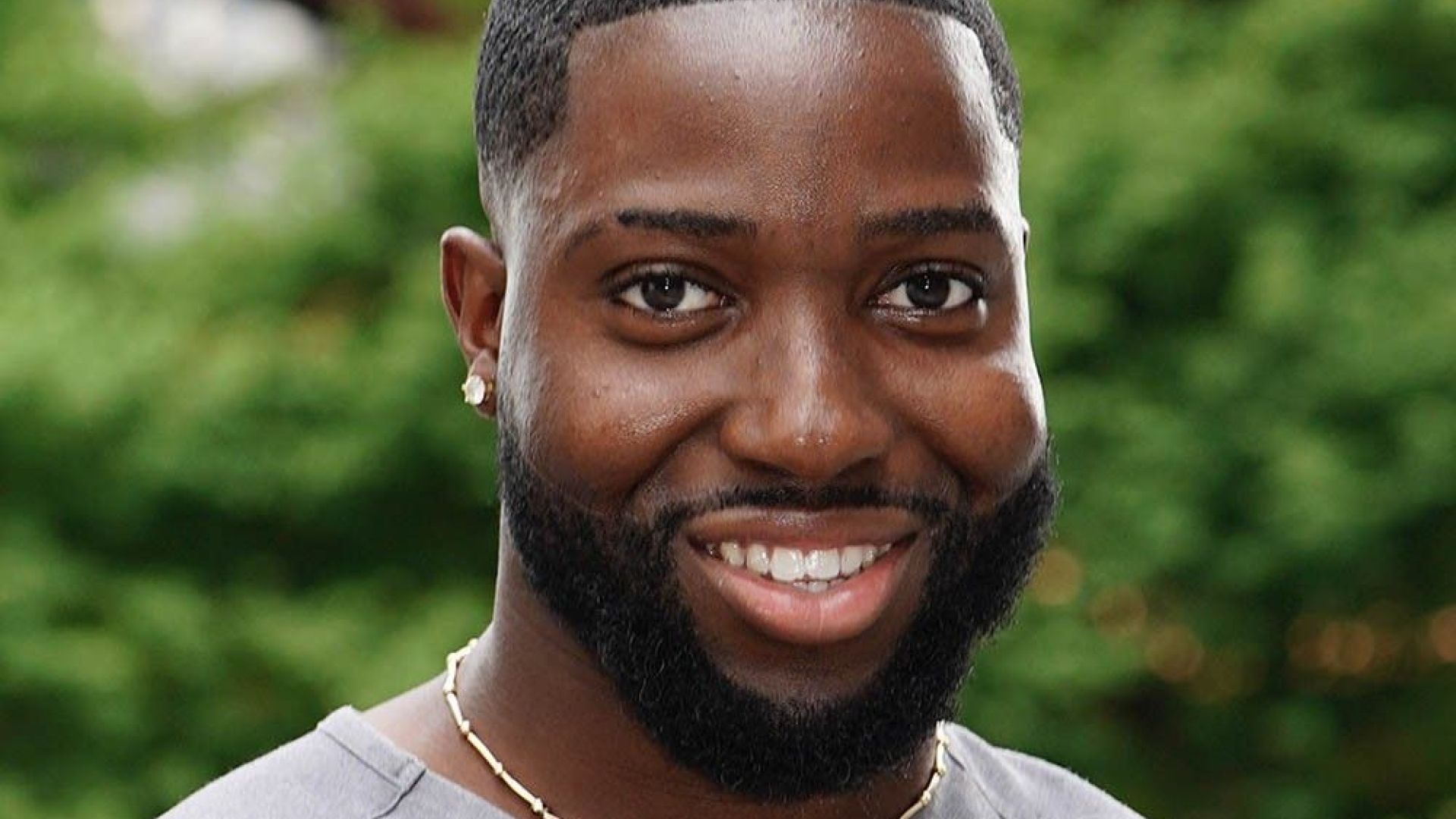 Jerone Osei smiling standing outdoors with greenery in the background.