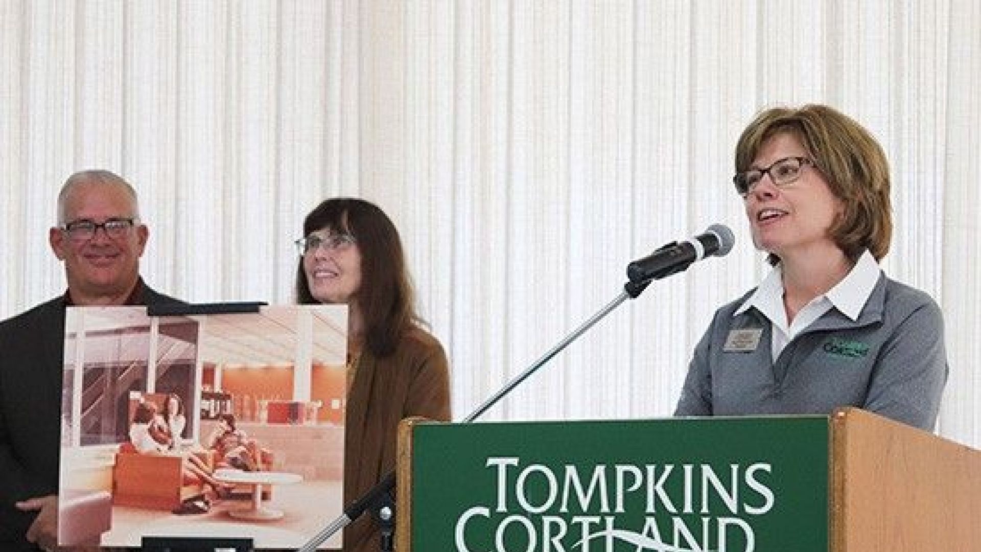 Amy Kremenek at a podium with two people holding a poster in the background.