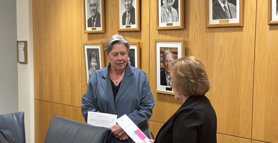 Woman stands as she is sworn in by the board chair next to her. 