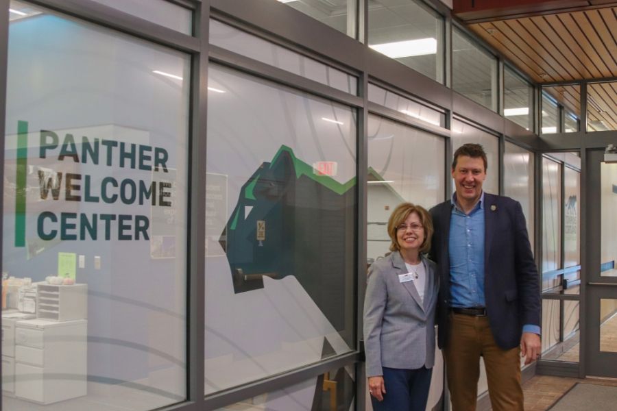 Two people in formal dress stand in front of a wrapped glass wall that has Panther Welcome center on it, and a giant Panther. 