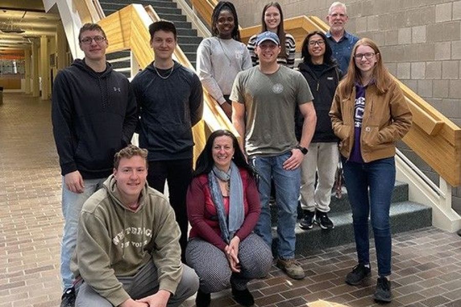 Group of ten students and faculty standing on and near staircase