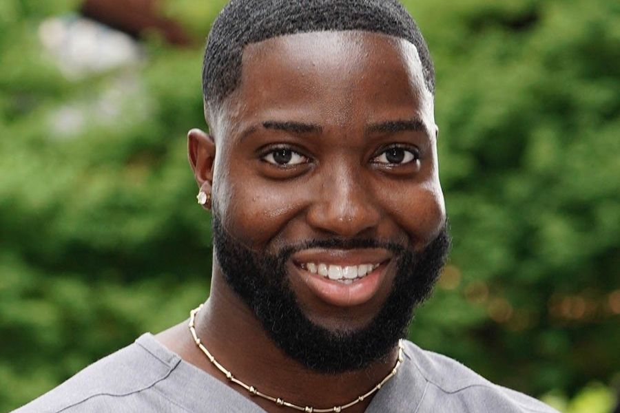 Jerone Osei smiling standing outdoors with greenery in the background.