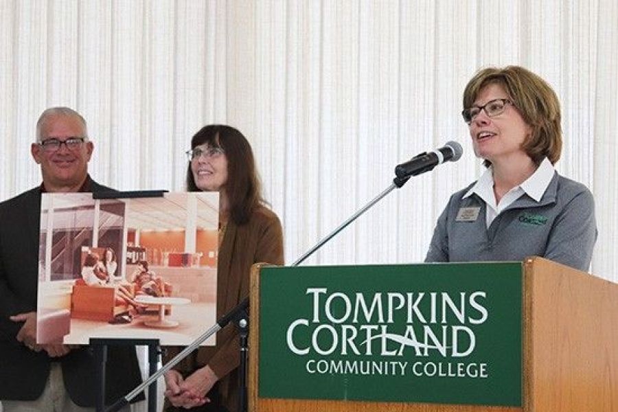 Amy Kremenek at a podium with two people holding a poster in the background.