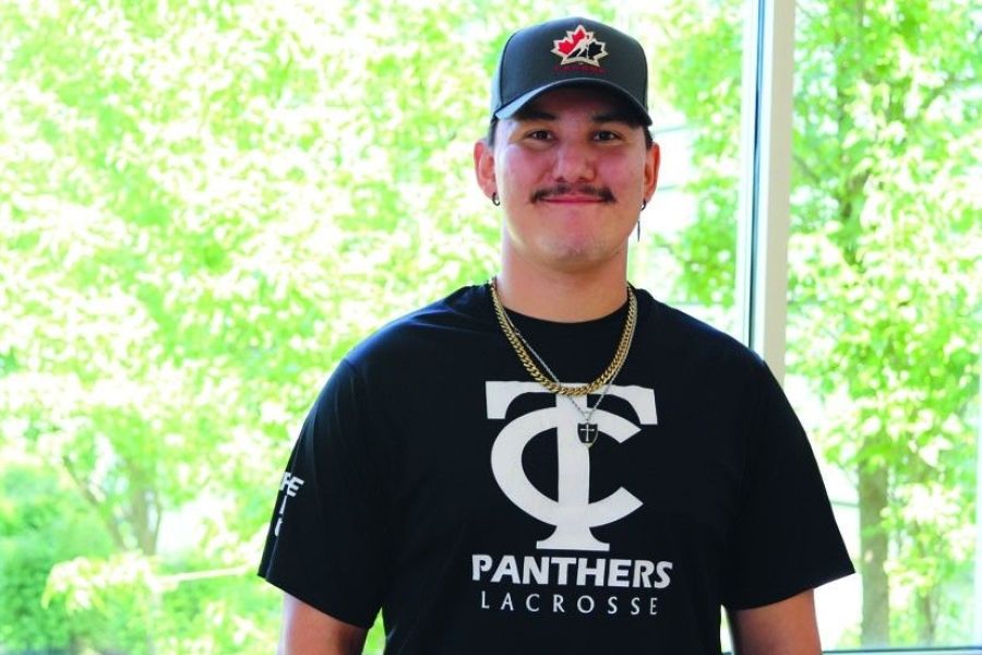Skylar Running Rabbit wearing a TC Panthers Lacrosse shirt in front of large windows with greenery in the background.